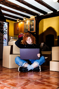 Woman with red hair experiencing stress during move, sitting on floor with laptop