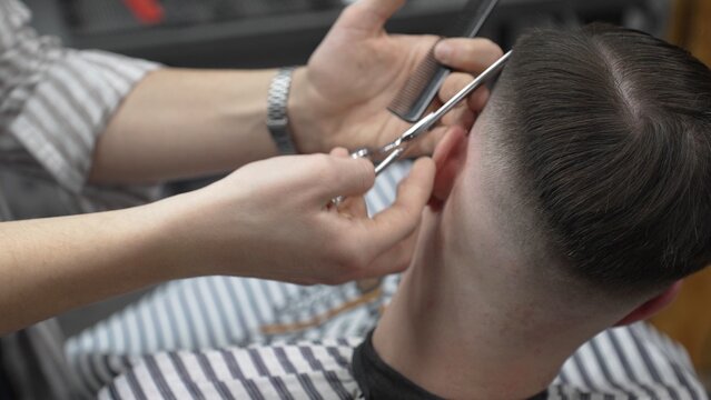Professional barber cutting client's hair with scissors and comb, creating a stylish fade in a modern barbershop, providing a high quality grooming service