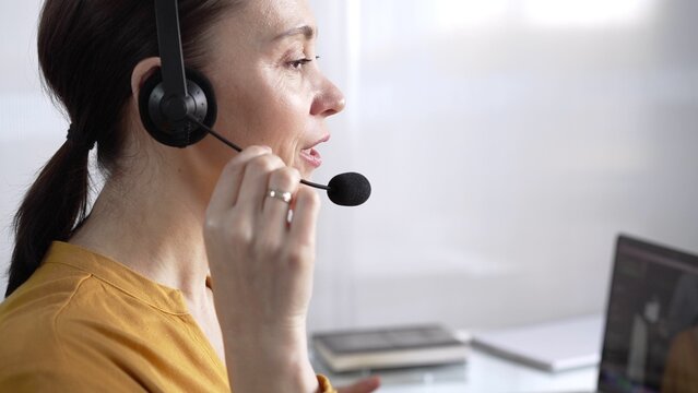 Focused female call center operator in yellow casual blouse is assisting clients online, providing customer support and answering inquiries. Call center concept