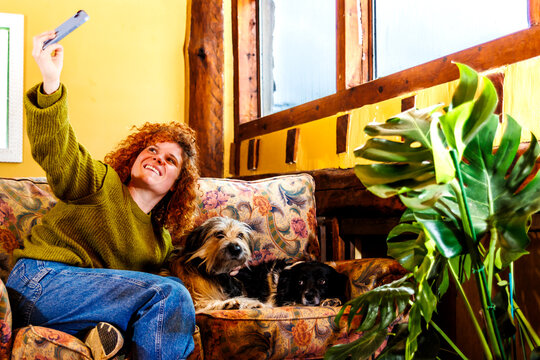 Happy woman taking selfie with loyal pet dogs relaxing on sofa at home