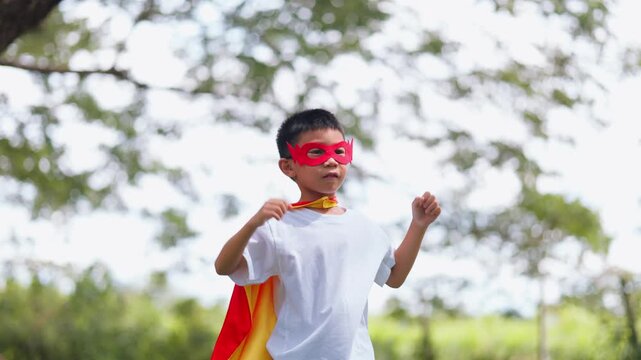 Cute Asian children playing superhero roleplay with colorful cape and mask running in outdoor green park. Kids imagination, creative future dream, and brave hero inspiration.
