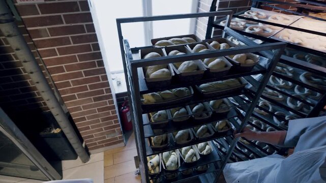 Baker in white uniform removes trays of rising dough from proofing cabinet, showcasing the continuous process of bread preparation in a well-lit bakery environment