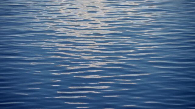 Serene blue ocean water surface featuring gentle ripples and soft waves with beautiful sunlight reflections creating a peaceful and tranquil aquatic scene perfect for meditation backgrounds.