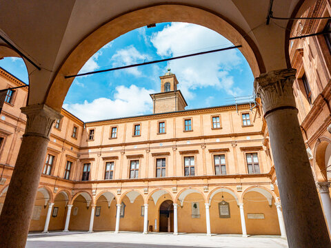 Palazzo dei Pio courtyard in Carpi, Italy, reflecting Renaissance architecture with its characteristic arcade, columns, and a central clock tower against a blue sky