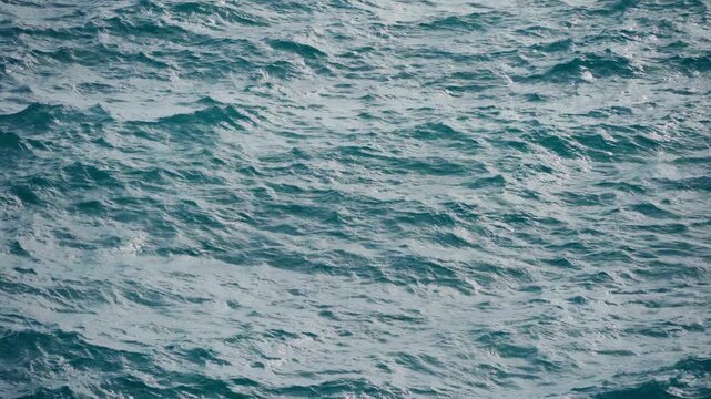 Choppy ocean water surface with deep blue and teal waves creating natural texture patterns. Windy conditions produce small whitecaps and ripples across the endless open sea.