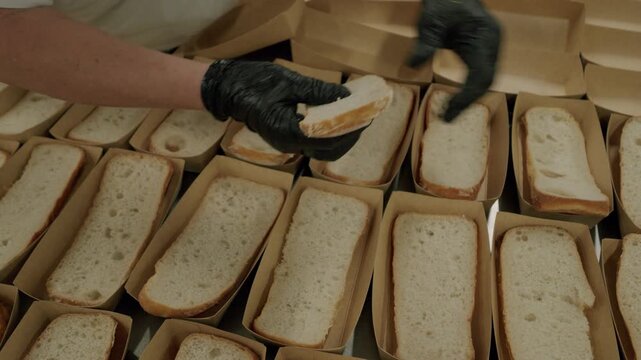 Individual wearing black gloves places slices of bread into cardboard trays, showcasing the organized arrangement of baked goods in a commercial kitchen setting
