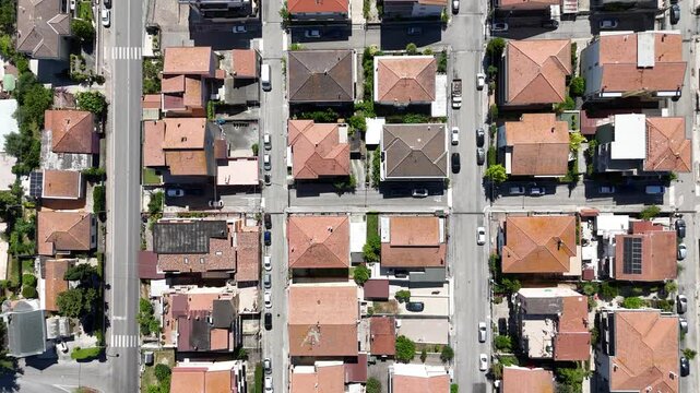 Top down aerial drone view of Roseto degli Abruzzi town residential streets and houses rooftops with parked cars during sunny day in Abruzzo Italy.