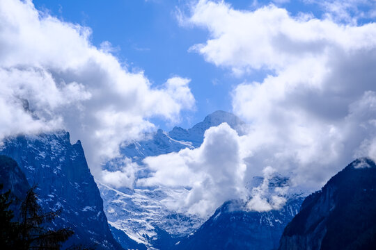 A stunning, high-altitude landscape photograph looking south from the alpine village of Wengen down into the iconic Lauterbrunnen Valley. The snow-shrouded peak of the massive Jungfrau mountain emerge