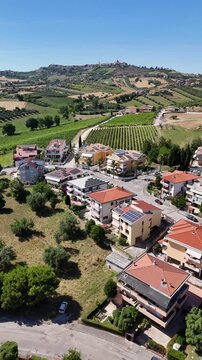 Vertical aerial drone view of Roseto degli Abruzzi town residential houses near green vineyards and scenic hills under blue sky in Abruzzo region Italy.