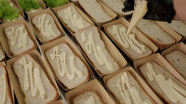 Preparation of sandwiches with fresh lettuce and mayonnaise spread on bread in a clean kitchen setting, showcasing the assembly process in a food preparation area