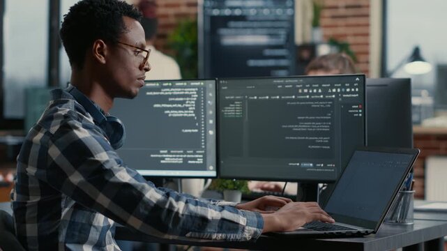 African American programmer develops interface concepts around programming data, using office collaboration to refine cloud software workflow and UI logic, while checking source code.