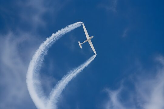 Aerobatic glider trailing clean vapor ribbon through tight vertical loop with blank wings soaring gracefully