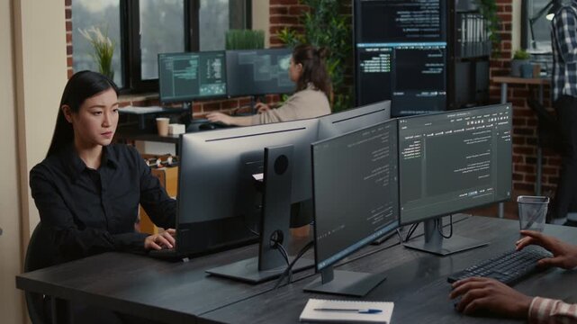 Two software developers collaborate at a workstation with running code screens, connecting programming workflow, data systems and teamwork, during a developer productivity task.