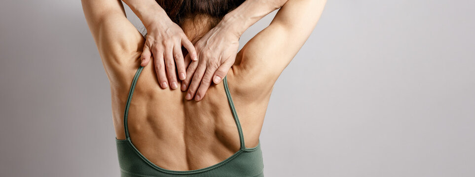 Woman holding upper hands back neck muscles, concept of pain, sport muscle tension and physiotherapy with copy space banner grey background
