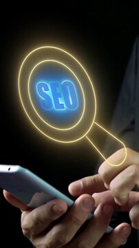 Vertical shot of person holding smartphone with finger pointing at glowing yellow SEO magnifying glass search icon. Cyber neon lighting, mobile search engine optimization and digital marketing concept