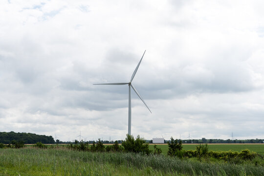 A modern wind turbine towers over rural land beneath a dramatic cloudy sky, symbolizing renewable energy, clean power, and sustainable electricity.