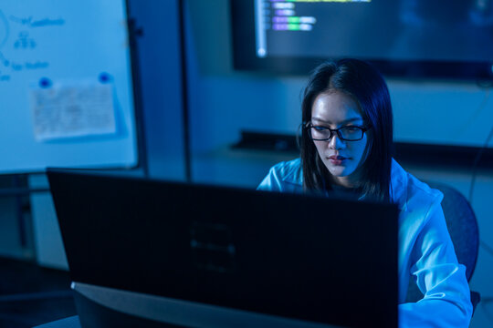 Asian female programmer coding on computer in dark office, Woman software developer typing code late at night, IT cyber security engineer working with male colleague, Tech data center hacker concepts
