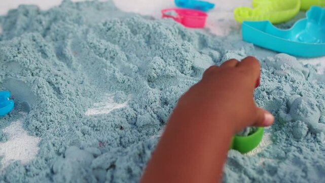 Child's Hands Playing with Blue Kinetic Sand and Colorful Plastic Toys
