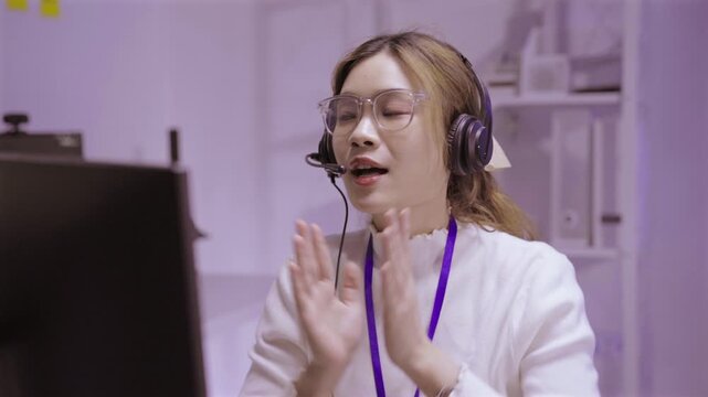 Asian woman IT support agent talking on online video call in dark office