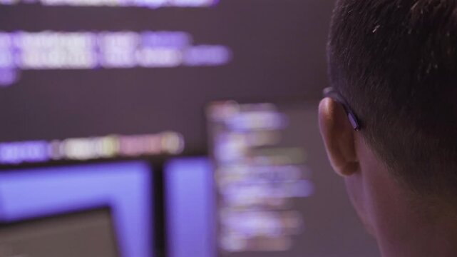 Programmer working on computer screen with code in dark room