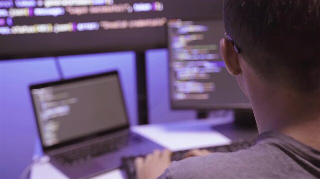 Programmer working on computer screen with code in dark room