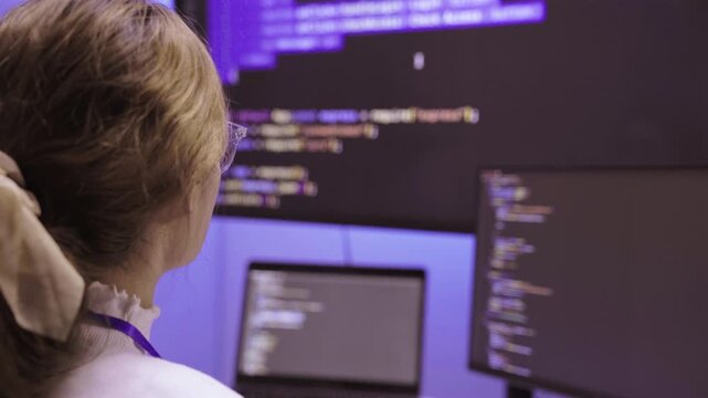 Female software developer writing code on computer screen in office