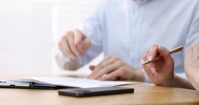 Insurance agent working with client and showing where to sign document at table in office, closeup