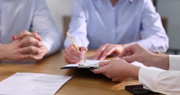 Insurance agent showing client where to sign document at table in office, closeup. Camera moving forward