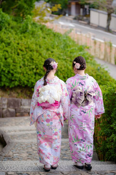 Two young women in yukata walking down stone steps in a traditional Japanese town.