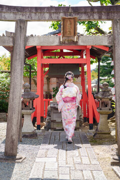 Young woman in pink yukata walking through a torii gate at a Japanese shrine.
