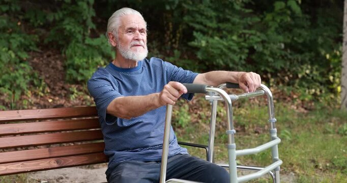 Elderly man with walking frame resting on bench in park