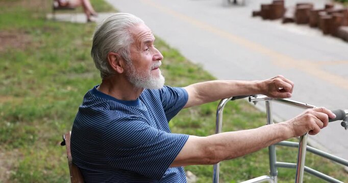 Elderly man with walking frame resting on bench in park