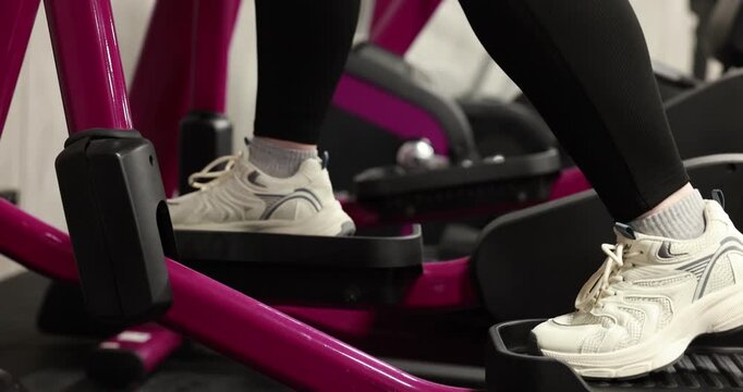Overweight woman exercising with elliptical trainer in gym, closeup