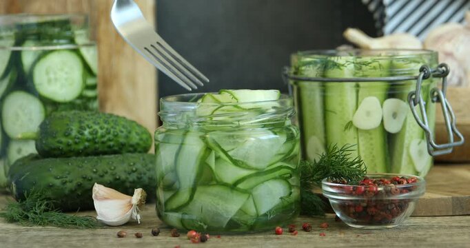 Woman taking pickled cucumbers from jar at wooden table, closeup