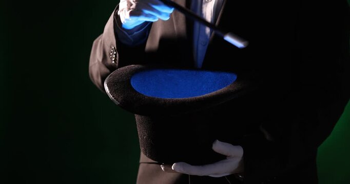 Magician showing trick with wand and top hat on stage, closeup