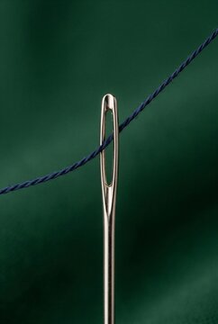 Needle with blue thread passing through the eye on green background  