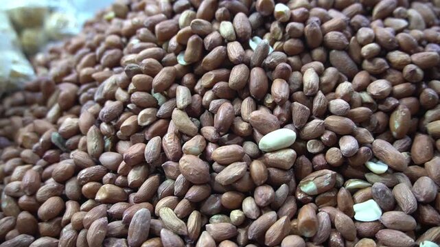 A massive pile of raw shelled peanuts displayed in a large mound for sale at a bustling traditional market