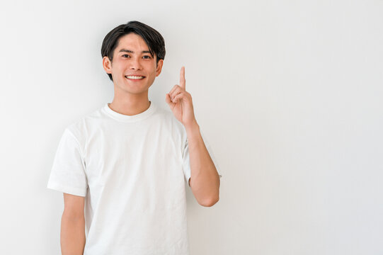 A young Asian man in a T-shirt pointing (point, introduction, guidance, recommendation, direction)