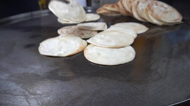 Parathas cook using metal tongs to flip flatbreads on a large hot metal griddle during food preparation