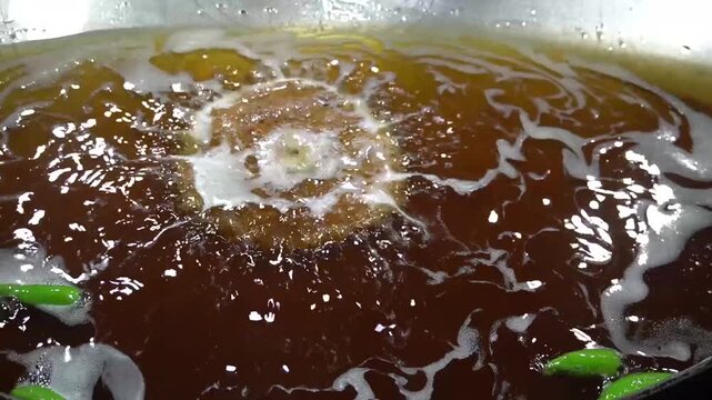 Hot oil bubbling and splashing aggressively in a large deep frying metal wok inside a commercial food kitchen, chapli kebab