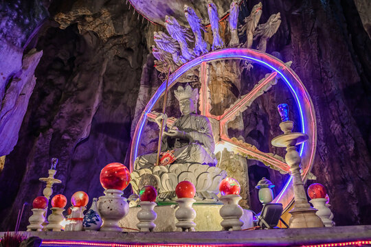 Sacred stone statue with neon wheel of dharma and naga guardians inside the mystical illuminated Am Phu cave of Marble Mountains in Da Nang Vietnam