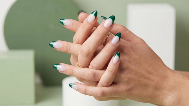 Hands with dark green French tip manicures are elegantly intertwined in front of geometric shapes to showcase a clean and modern aesthetic for professional beauty branding.