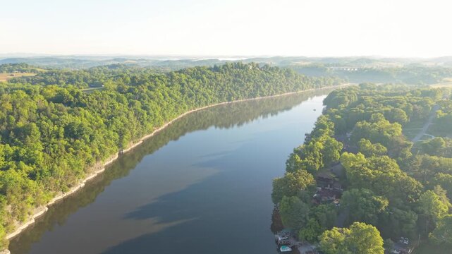 Aerial perspective of a calm river meandering through verdant hills and forests in Johnson City, Tennessee, highlighting the peacefulness of the natural environment and the clear blue sky above