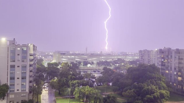 Static rooftop view of a lightning bolt hitting the ground during a hurricane in Miami. Heavy rain, wind-bent trees, purple sky flash. Authentic thunder and rain sound. Unedited 4K.