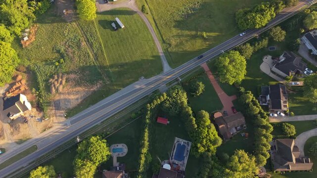 Aerial perspective of a suburban area in Johnson City, Tennessee, highlighting residential houses, lush green lawns, winding roads, and a swimming pool, with open fields visible in the distance