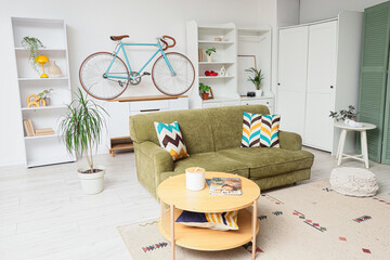 Obraz premium Modern living room interior with a green sofa, wooden coffee table, and a bicycle mounted on the wall