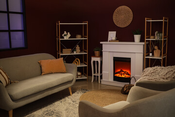 Obraz premium Cozy living room interior with a lit electric fireplace, comfortable sofa, and decorative shelves at night