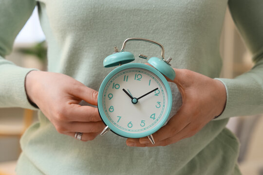 Woman setting time on alarm clock at home, closeup. Daylight saving time concept