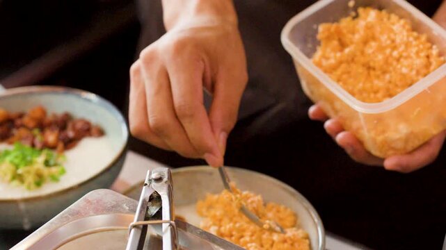Chef Hands Adding Toppings to Asian Congee Porridge Bowl