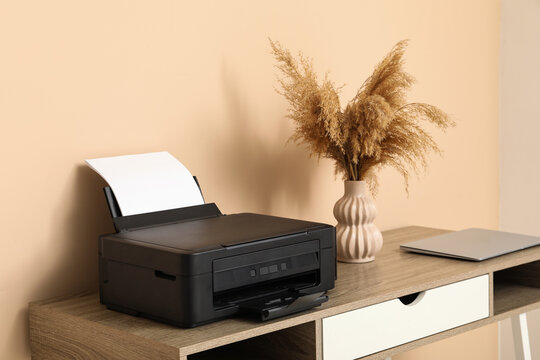 Modern printer and laptop on table near beige in home office